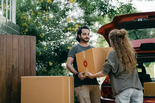 Two people loading essential moving day survival kit and first night boxes into the back of a red car, preparing to keep important items within easy reach.