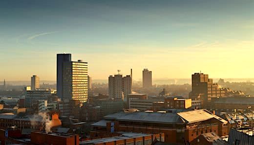 Skyline of Leicester city at sunrise, featuring a mix of modern high - rise buildings and older brick structures under a clear sky with a warm golden glow.