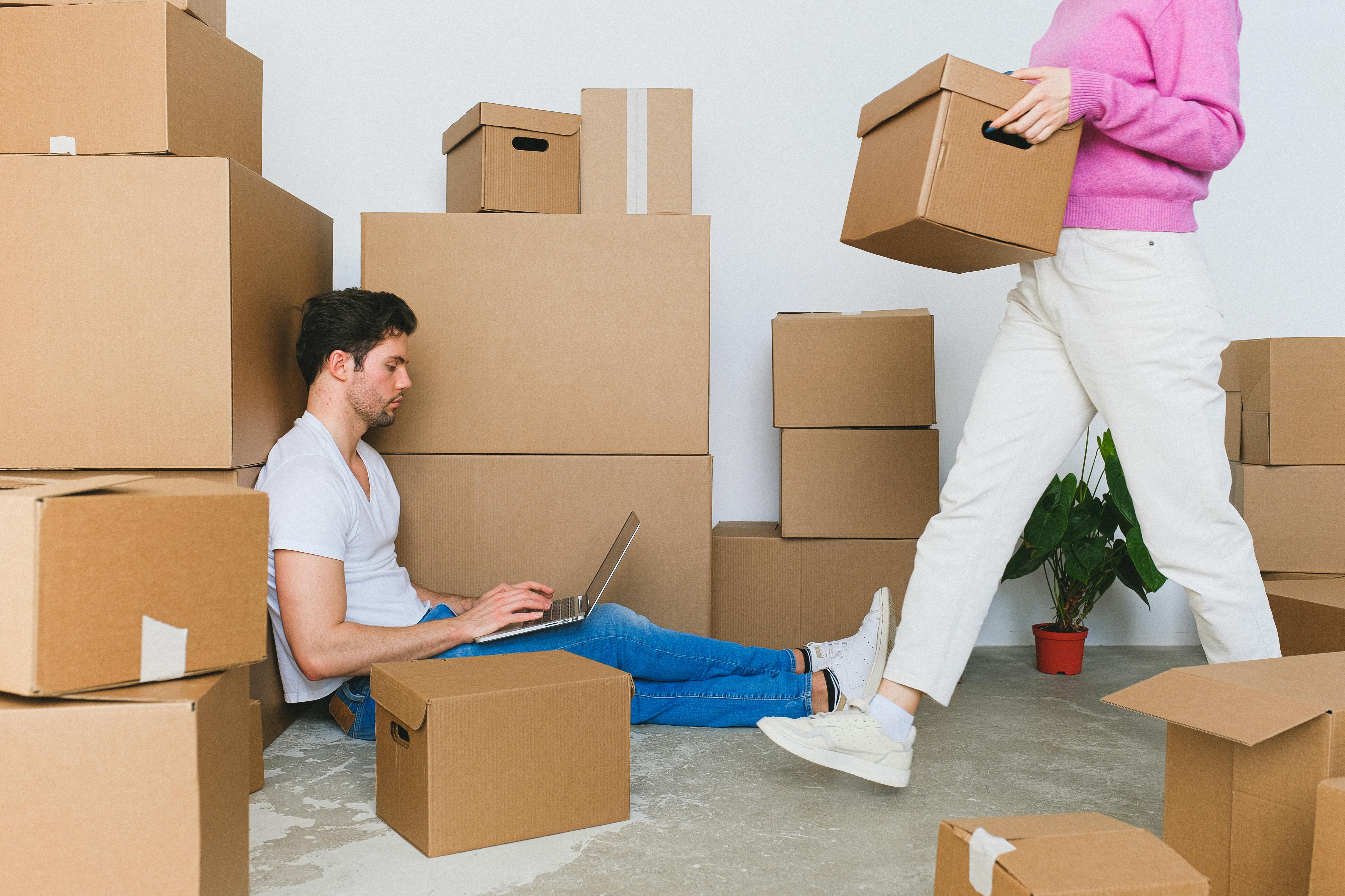 Couple planning house moving with laptop surrounded by cardboard moving boxes, illustrating comprehensive UK house moving support and move planning consultation