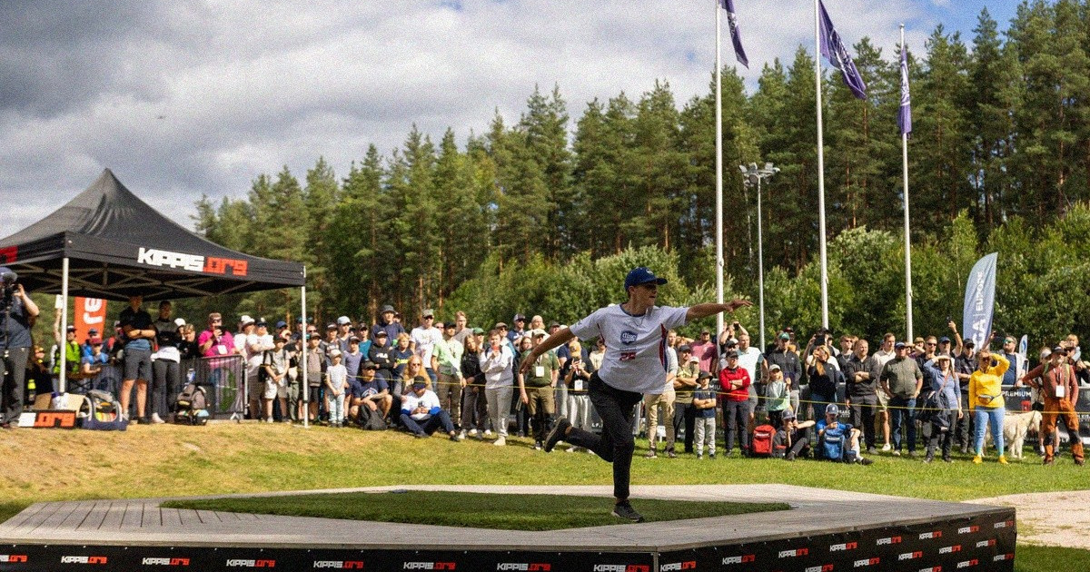 Frisbeegolfpelaaja heittää kiekkoa yleisön seuratessa kilpailua.