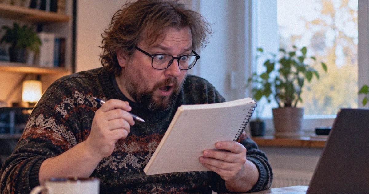 Silmälasipäinen mies tarkastelee muistikirjaansa kynä kädessään.
