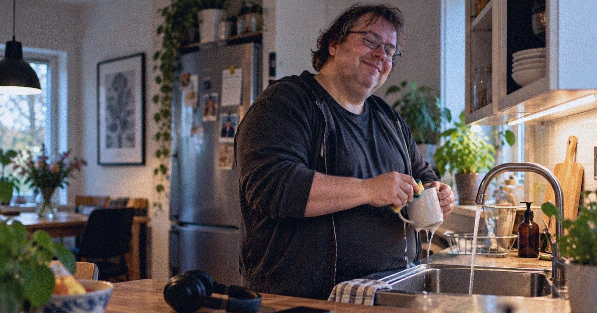 Mies pesee mukia keittiössä ja hyräilee kuulokkeiden ollessa pöydällä.
