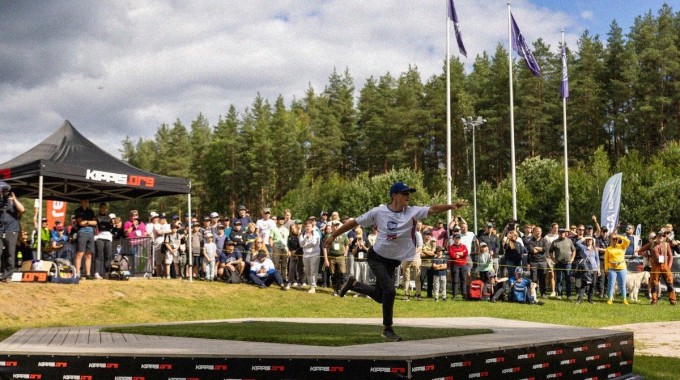 Frisbeegolfpelaaja heittää kiekkoa yleisön seuratessa kilpailua.