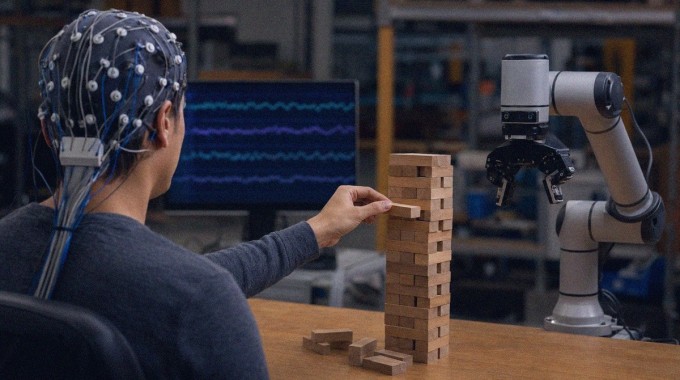 EEG-laitetta käyttävä robottikouluttaja irrottaa palikkaa puutornista robottikäden vieressä