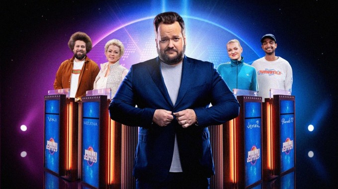 Kolme kilpailijaa ja juontaja sinisävyisessä televisiotietovisailun studiossa.