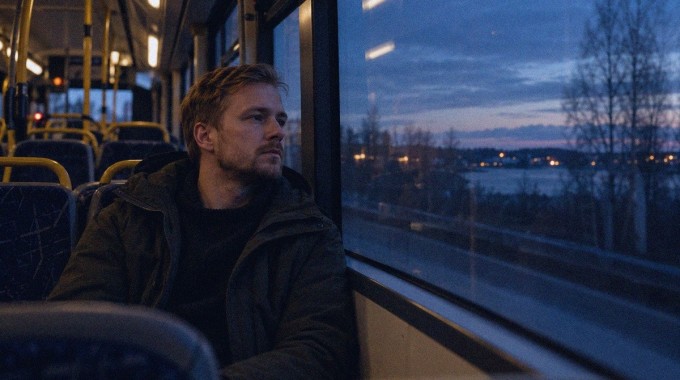 Mies istuu iltahämärässä bussin ikkunan vieressä mietteliäänä.