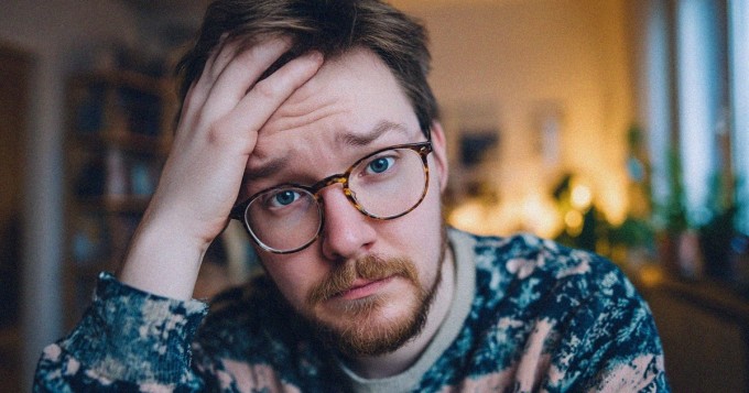 Työvaatteisiin pukeutunut aikuinen katsoo epävarmana perheen kalenteria ja kotitöitä keittiössä