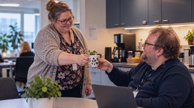 Nainen tuo kahvikupin työtoverilleen toimiston keittiössä.