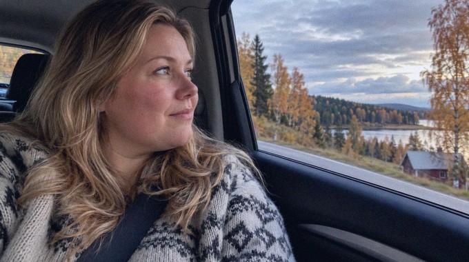 Matkustaja katselee syksyistä maisemaa auton ikkunasta maantiellä.
