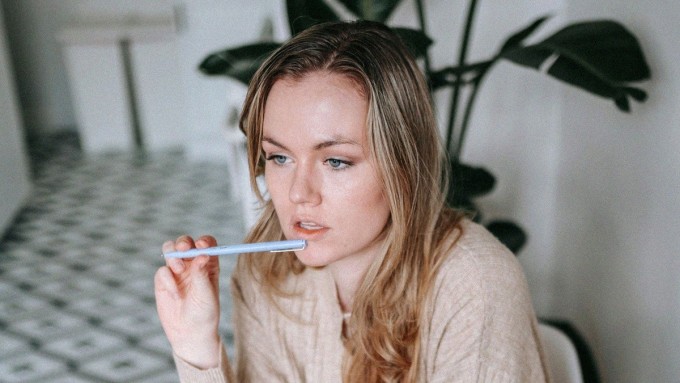 Mietteliäs nainen istuu tietokoneen ja muistikirjojen ääressä.