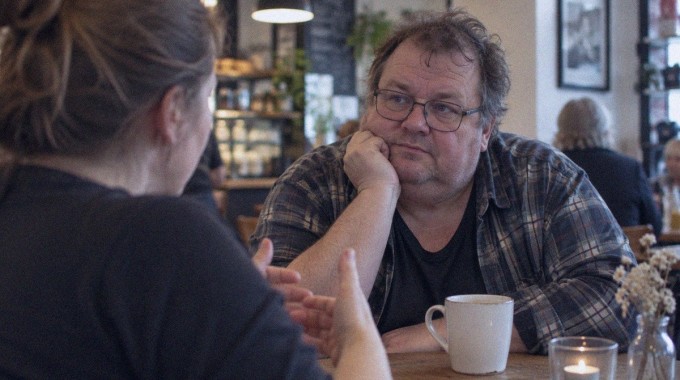 Rauhallinen aikuinen kuuntelee keskustelukumppania kahvilassa.