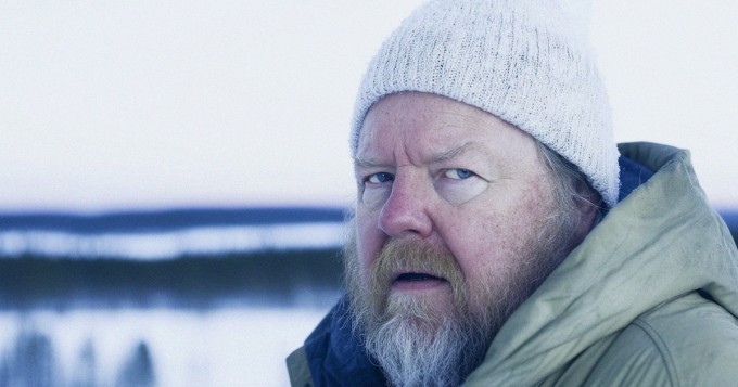 Kesämatkailijat vaeltavat viileässä säässä pohjoismaisen järvimaiseman äärellä.