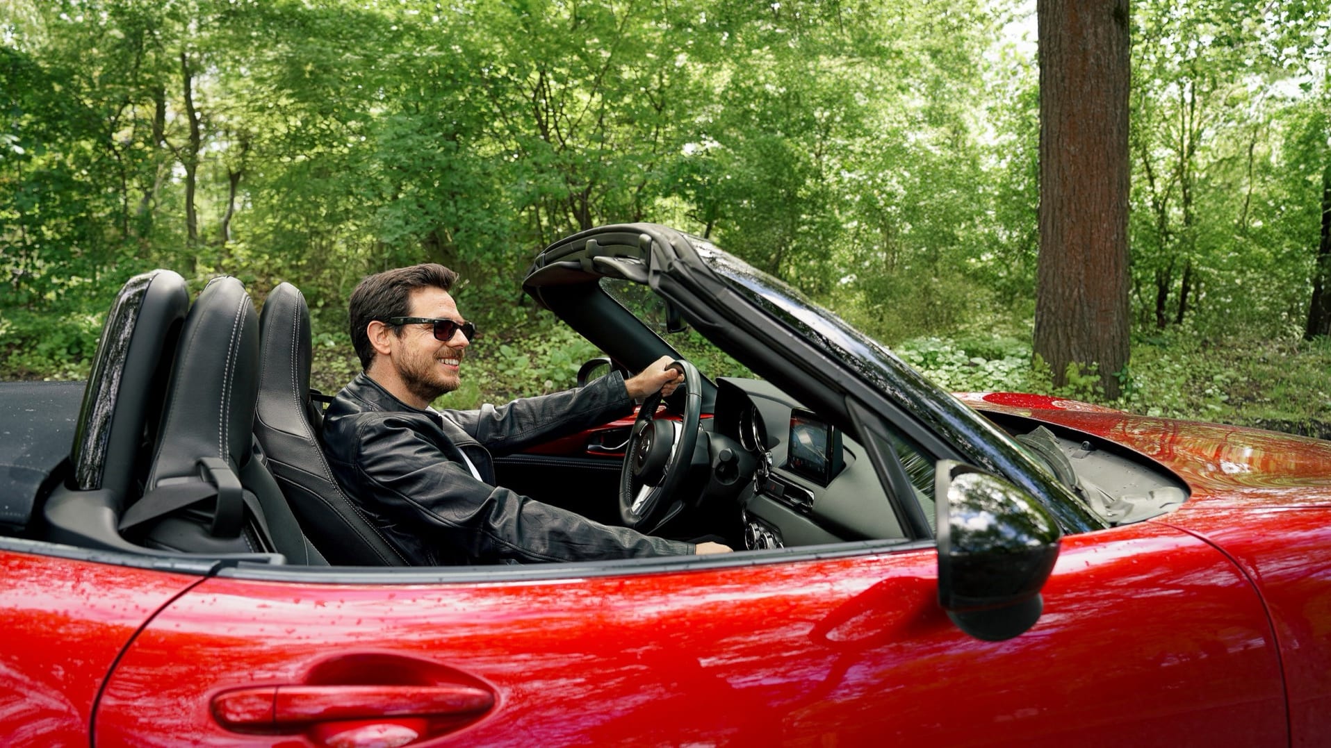 Ein Mann steht telefonierend neben einem Mazda MX 5 von FINN.