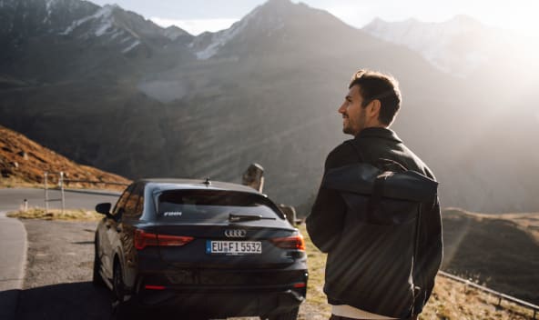 Ein Mann steht in den Bergen hinter seinem FINN Auto.