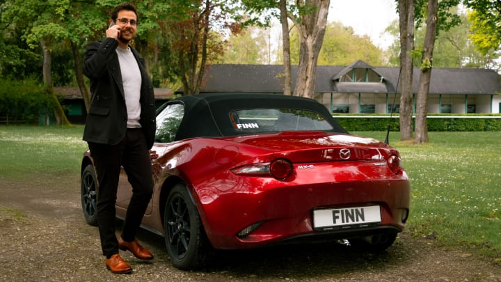 Ein Mann steht telefonierend neben einem Mazda M