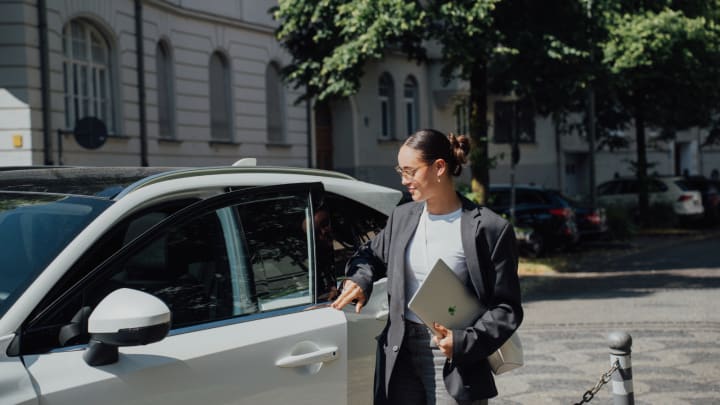 Frau schließt Autotür mit Laptop in der Hand.