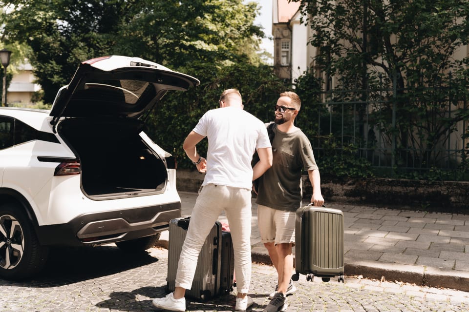 Zwei Männer räumen im Sommer Koffer in den Kofferraum eines Nissan.