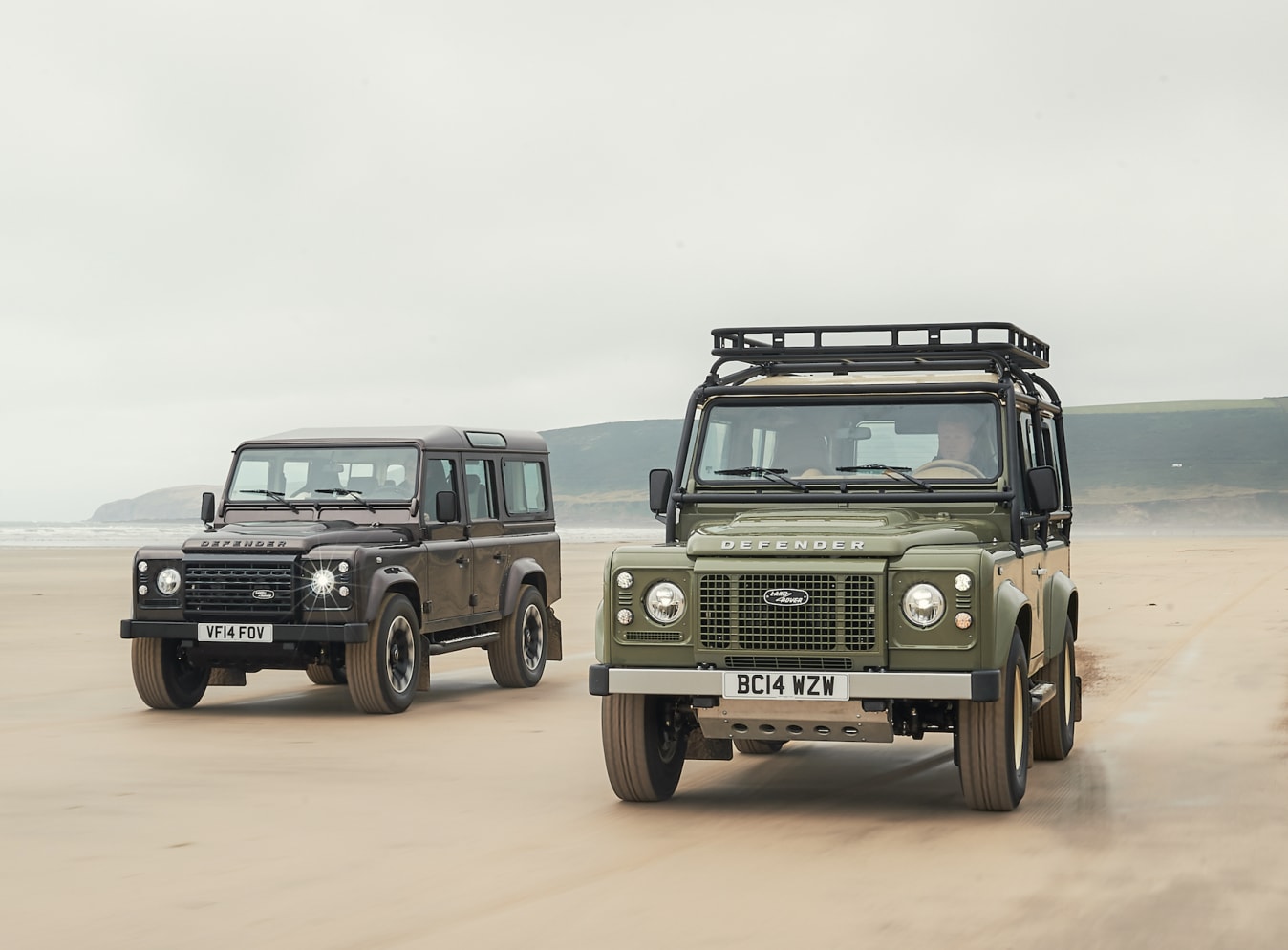 Zwei Land Rover Defender, die am Strand fahren.