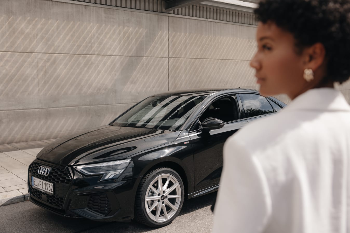 Ein schwarzer Audi A3 mit einer Frau im Vordergrund.