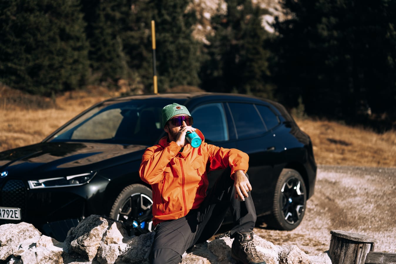 Mann in Wanderausrüstung sitz vor einem BMW.