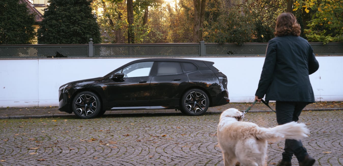 Ein Mann läuft mit seinem Hund auf einen BMW von FINN zu.