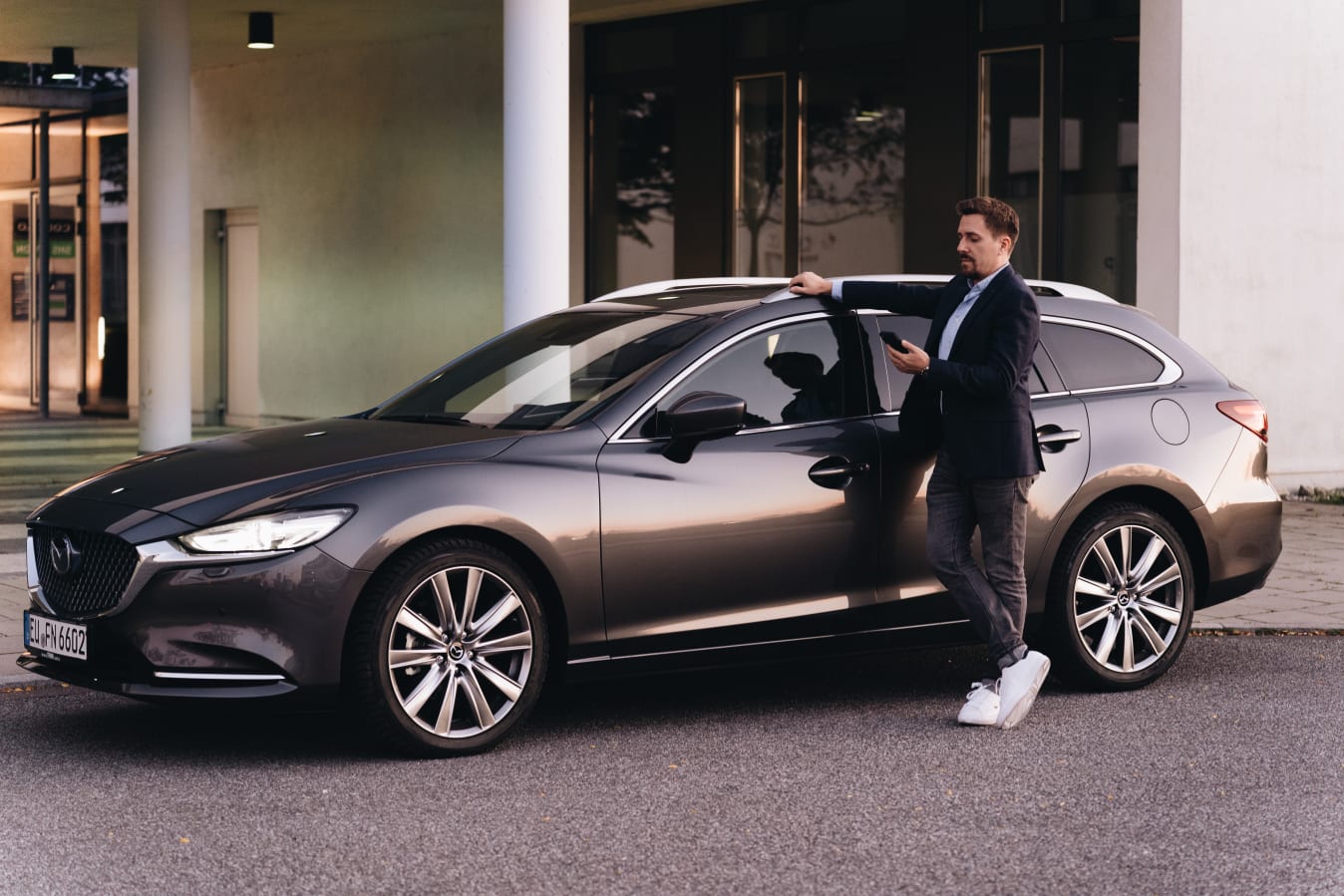 Ein Mann steht neben einem Mazda von FINN und schaut auf sein Handy.