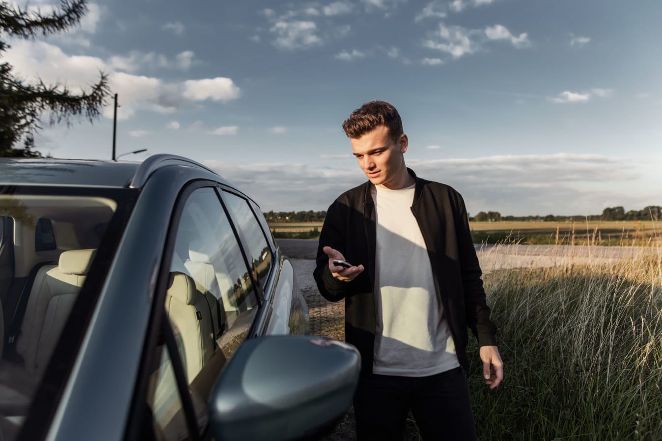 Eine Person steht mit dem Autoschlüssel in der Hand neben einem Auto an einem Feldweg.
