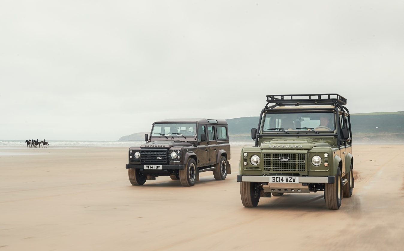 Zwei Land Rover Defender, die am Strand fahren.