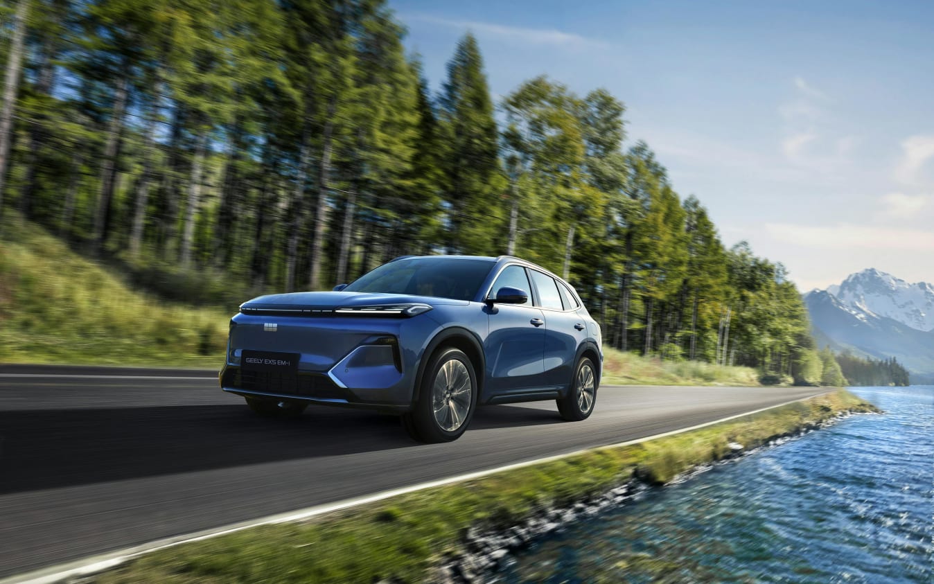 Ein blauer Geely Starray EM-i fährt auf einer Straße am Wald entlang.
