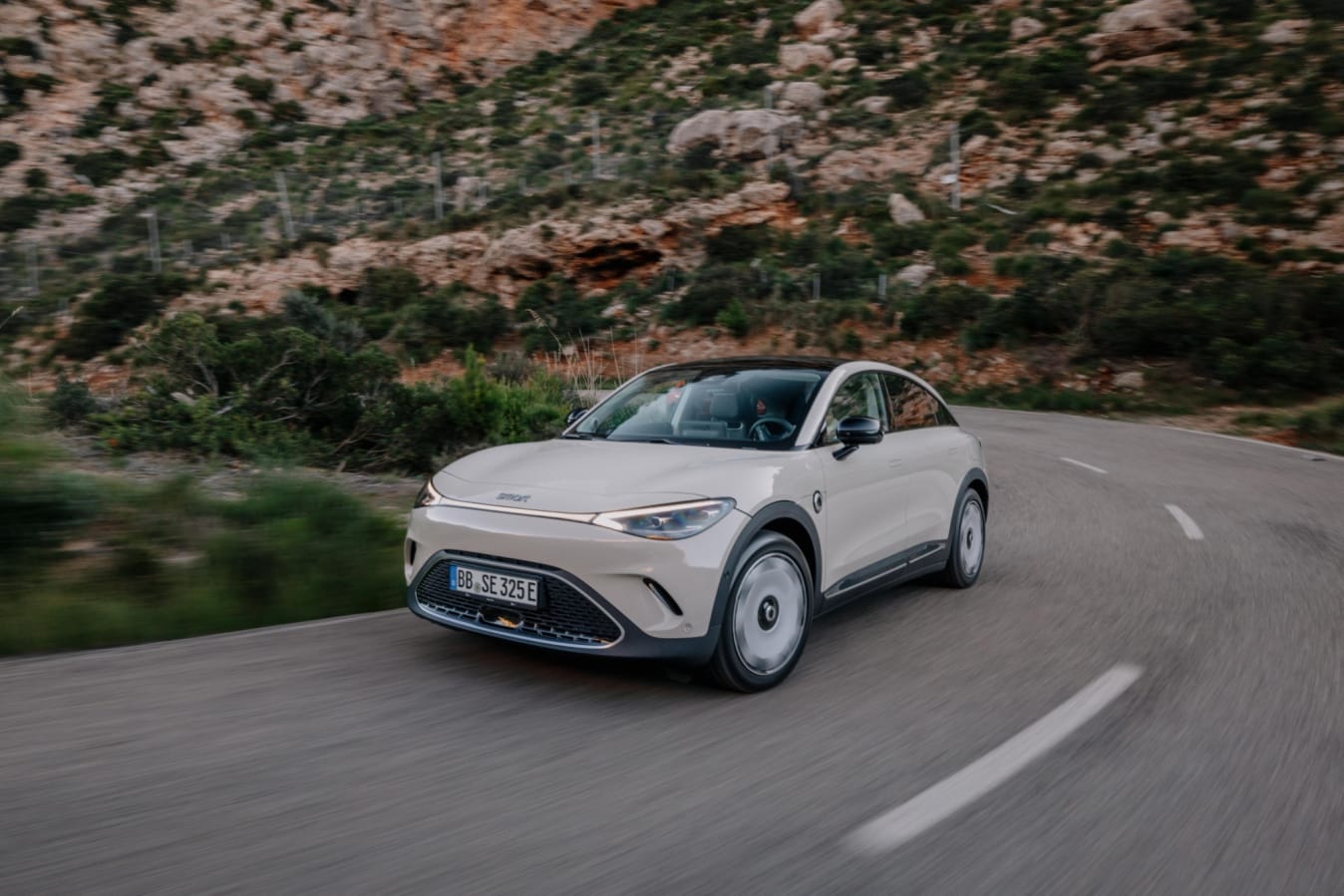 Ein beiger smart #5 fährt eine kurvige Bergstraße entlang.