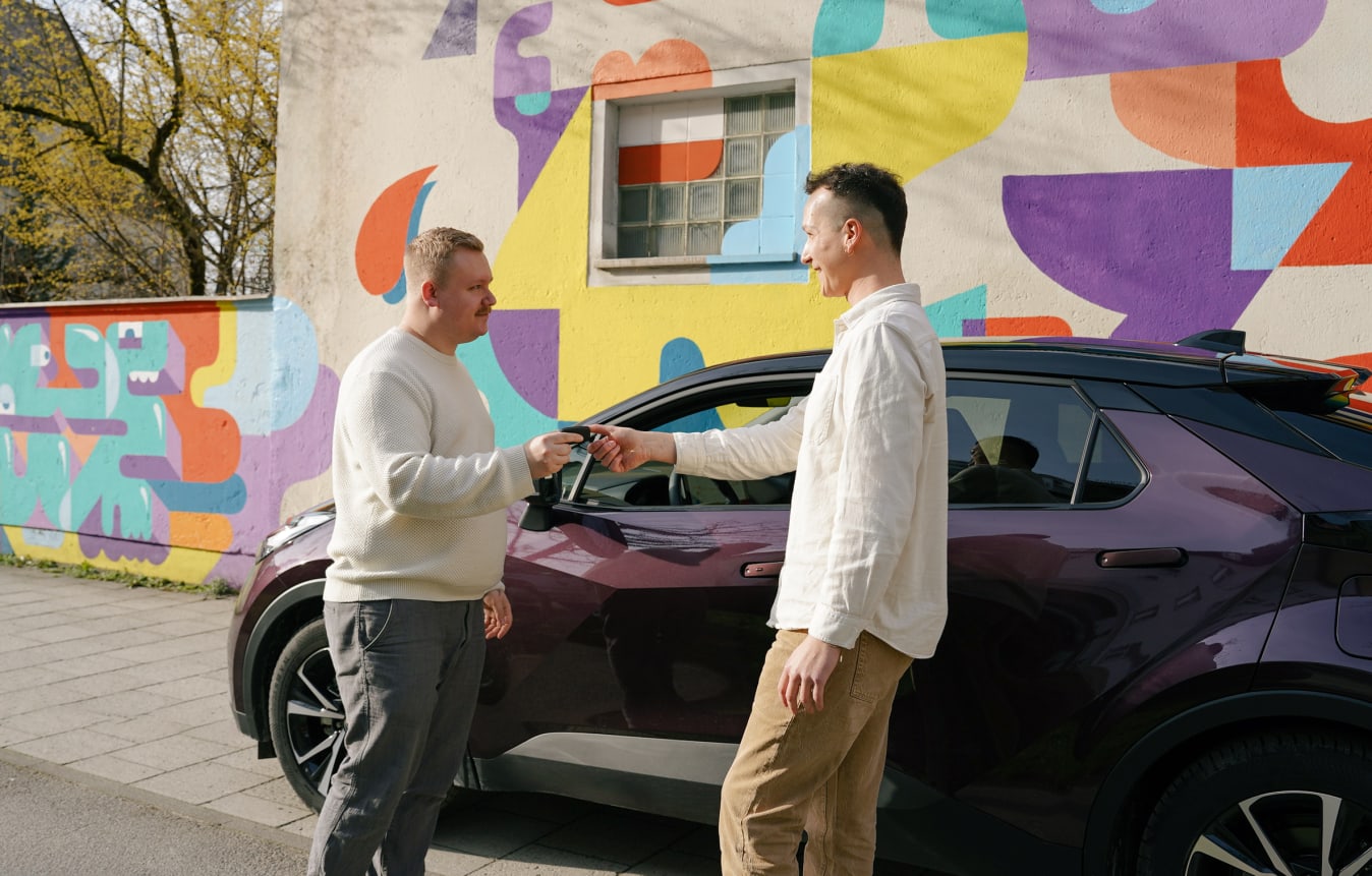 Ein Mann übergibt einem anderen den Autoschlüssel eines Toyota C-HR, der im Hintergrund steht.