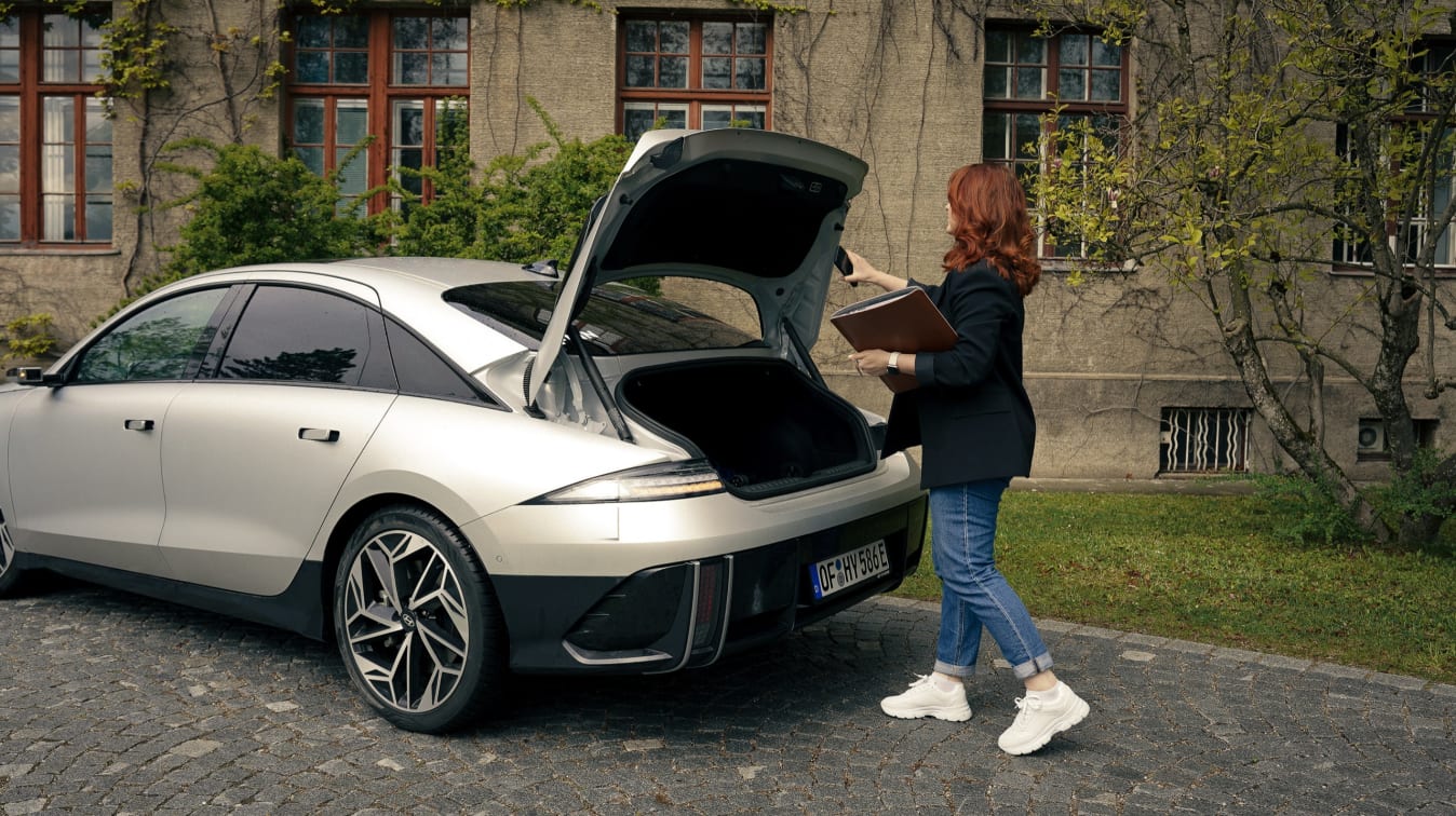 Eine Frau steht telefonierend und mit einer Mappe am geöffneten Kofferraum eines IONIQ 6.