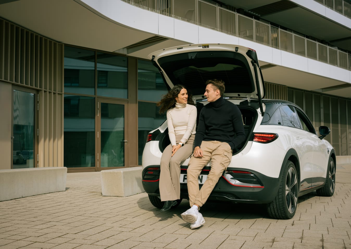 Eine Frau und ein Mann sitzen vorne im geöffneten Kofferraum eines smart #3.