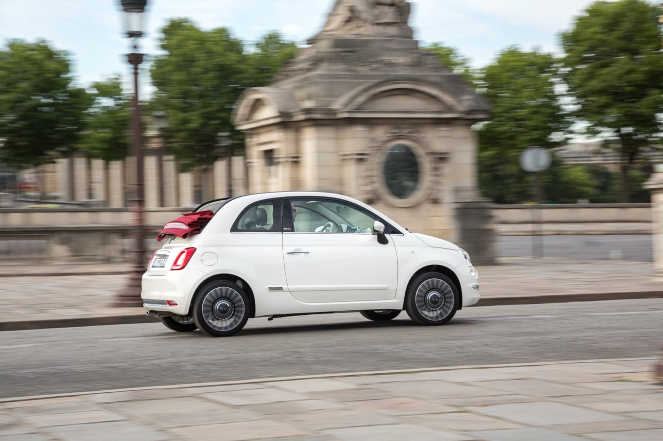 Ein weißes Fiat 500 Cabrio fährt auf der Straße.