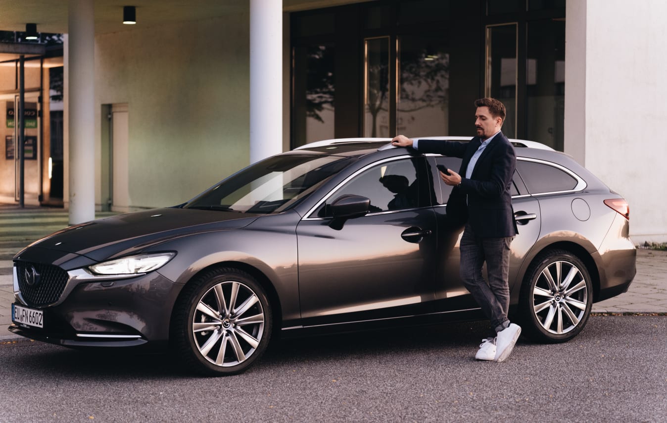 Ein Mann steht mit seinem Handy in der Hand vor seinem FINN Auto.