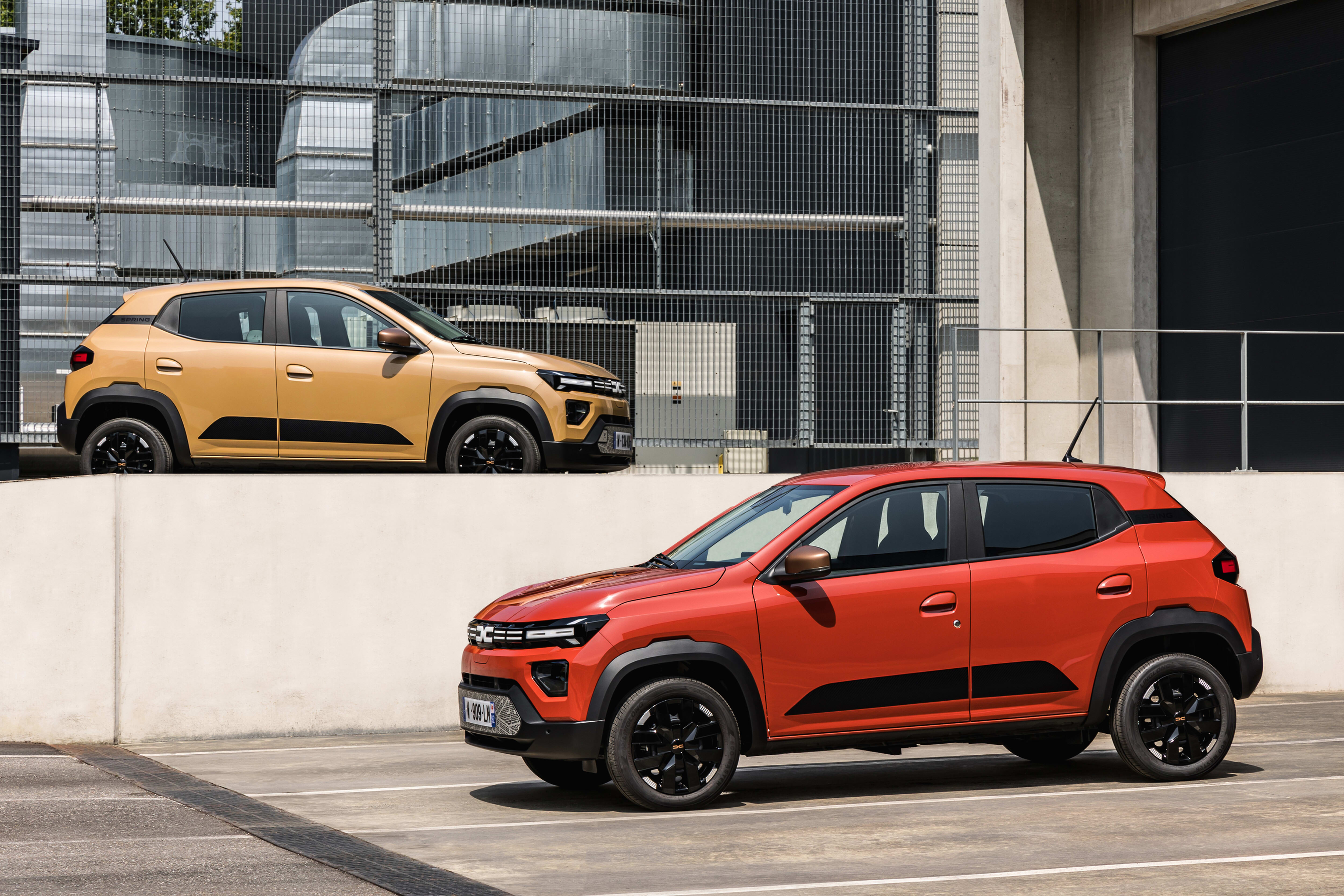 Ein orangener und ein roter Dacia Spring.