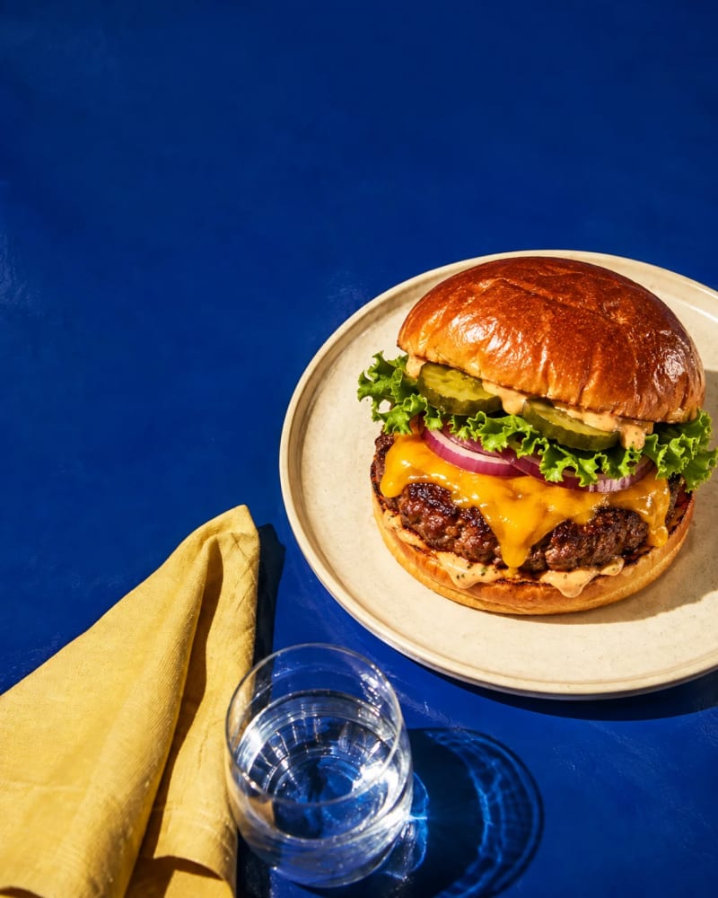 A juicy cheeseburger with a toasted brioche bun on a vivid blue restaurant table