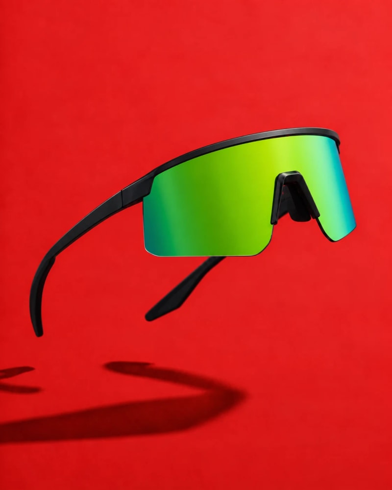 Minimal black cycling sunglasses with a rimless lime-green shield lens against a red background