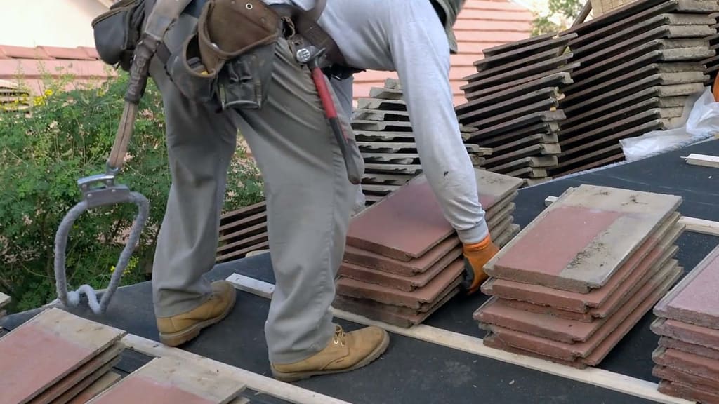 Our roofer leans over to pick up a stack of tiles as part of their work on this project.