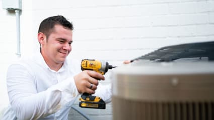 Having just completed a Fresno AC tune-up, our technician uses a cordless drill to fasten the condenser back together.