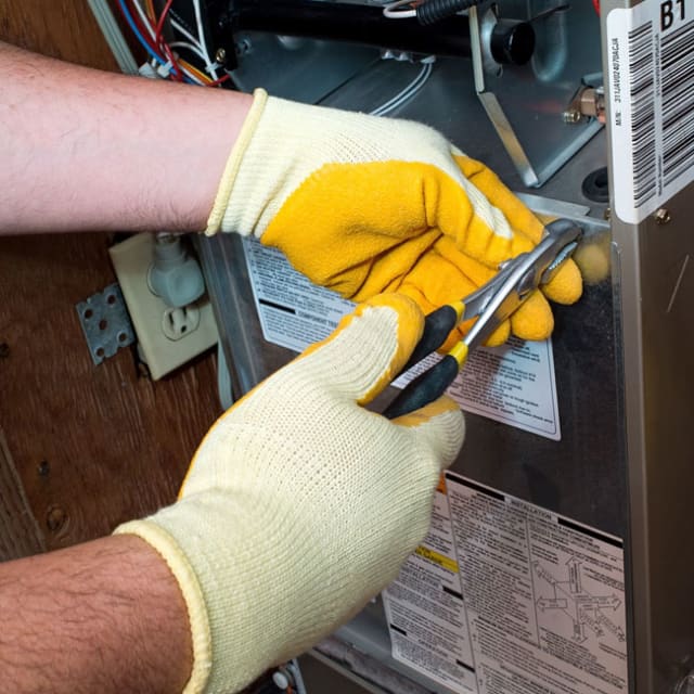 During a furnace tune-up in Chicago, our tech uses pliers to access a gas furnace to start the cleaning process.