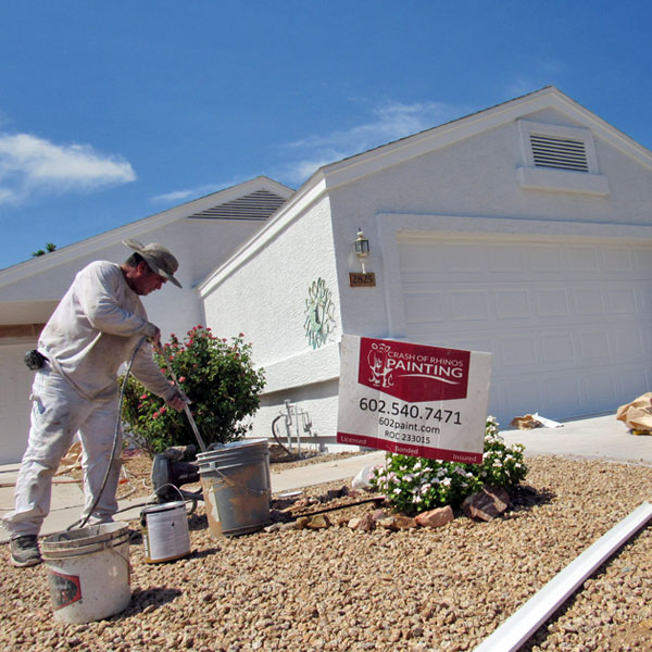 A Crash of Rhinos painter gets paint from a bucket as they prepare to repaint this home in Mesa, Arizona.