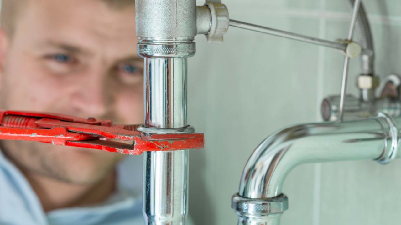 A Chicago plumber on the King team uses a wrench to adjust the drain pipe underneath a home's bathroom sink, fixing a leak.