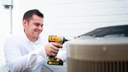Having just completed a Fresno AC tune-up, our technician uses a cordless drill to fasten the condenser back together.