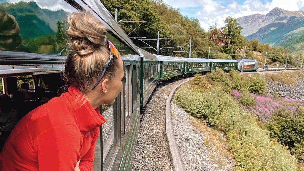 Kvinne i rødt på Flåmsbana, smiler mot lanskapet utenfor .