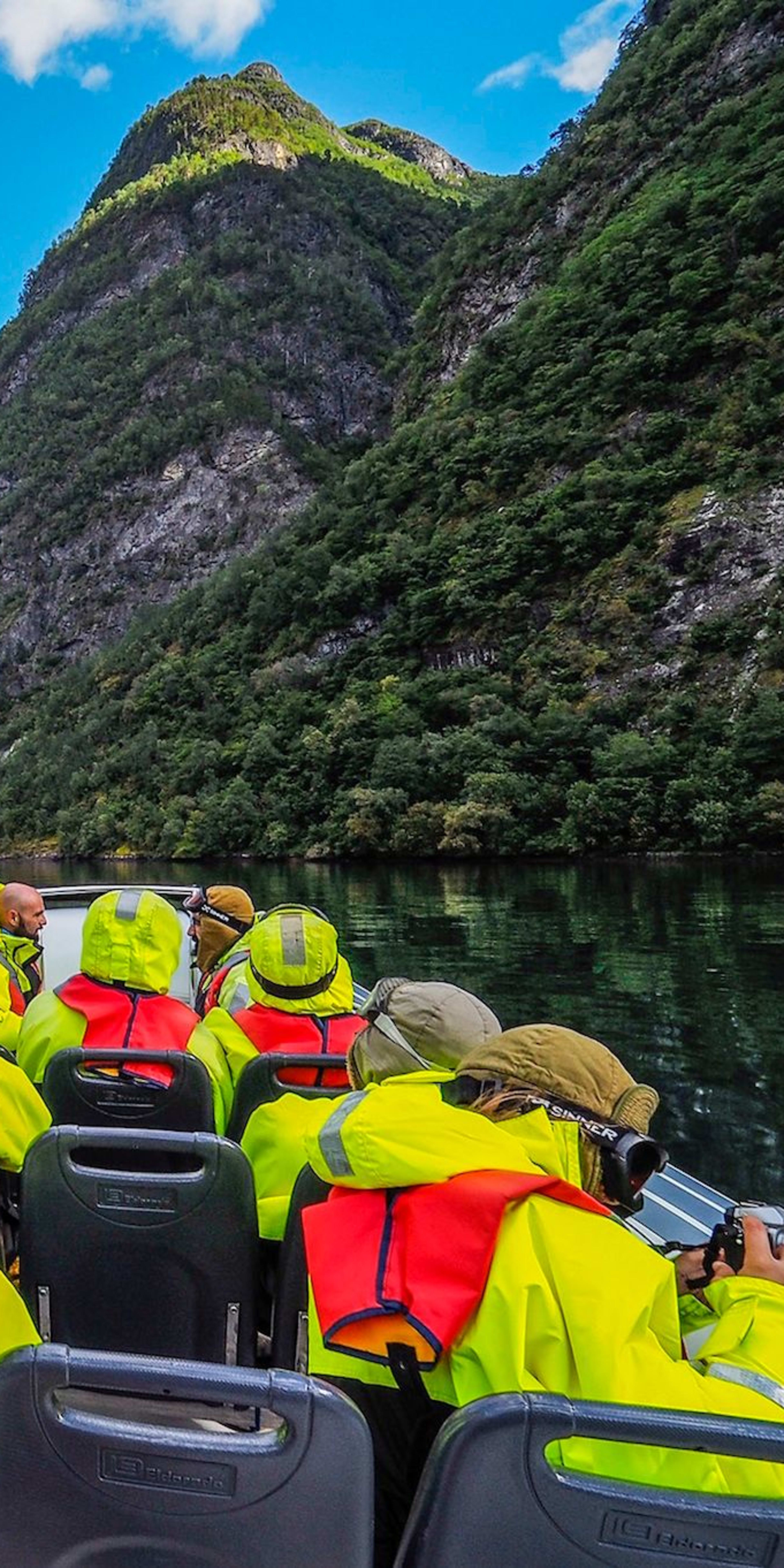 Menschen auf einer Rib-Boot-Safari im wunderschönen Nærøyfjord mit spiegelnden Klippen und bewölktem Himmel.