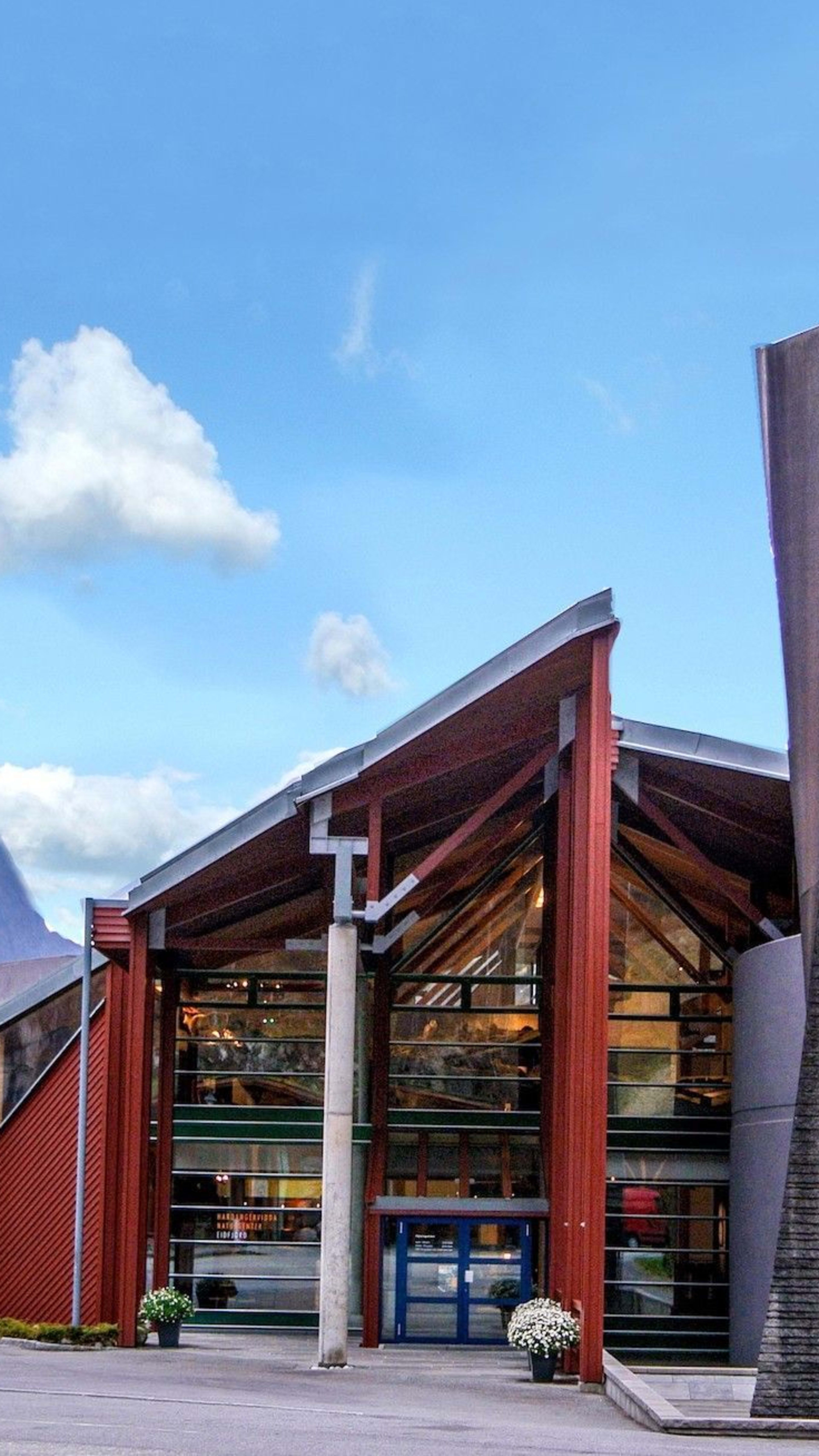 Modernes rotes Glasgebäude im norwegischen Naturzentrum Hardanger, zwischen Bergklippen gelegen.