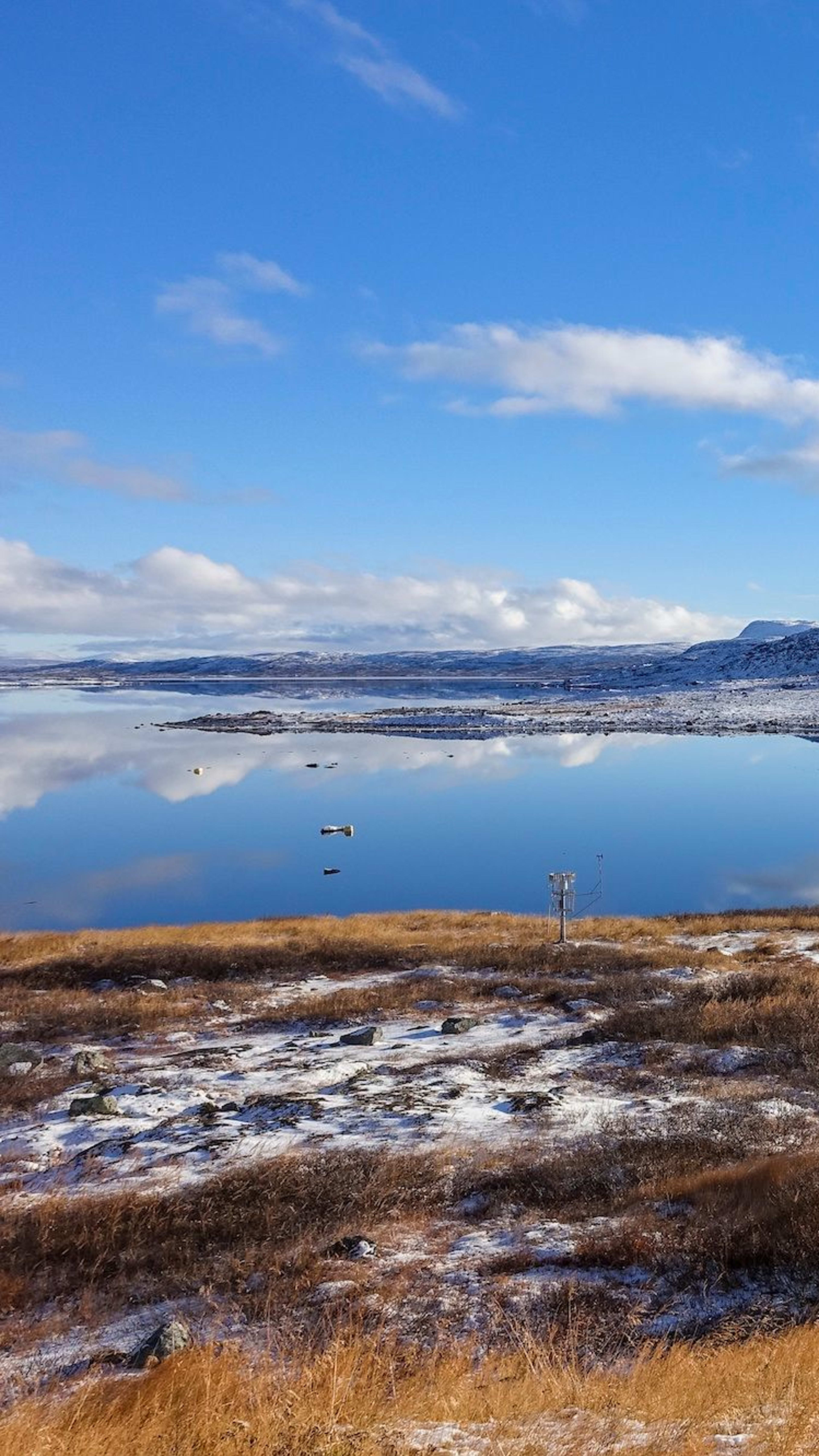 Holzhütten am See im verschneiten Gebirge unter blauem Himmel.
