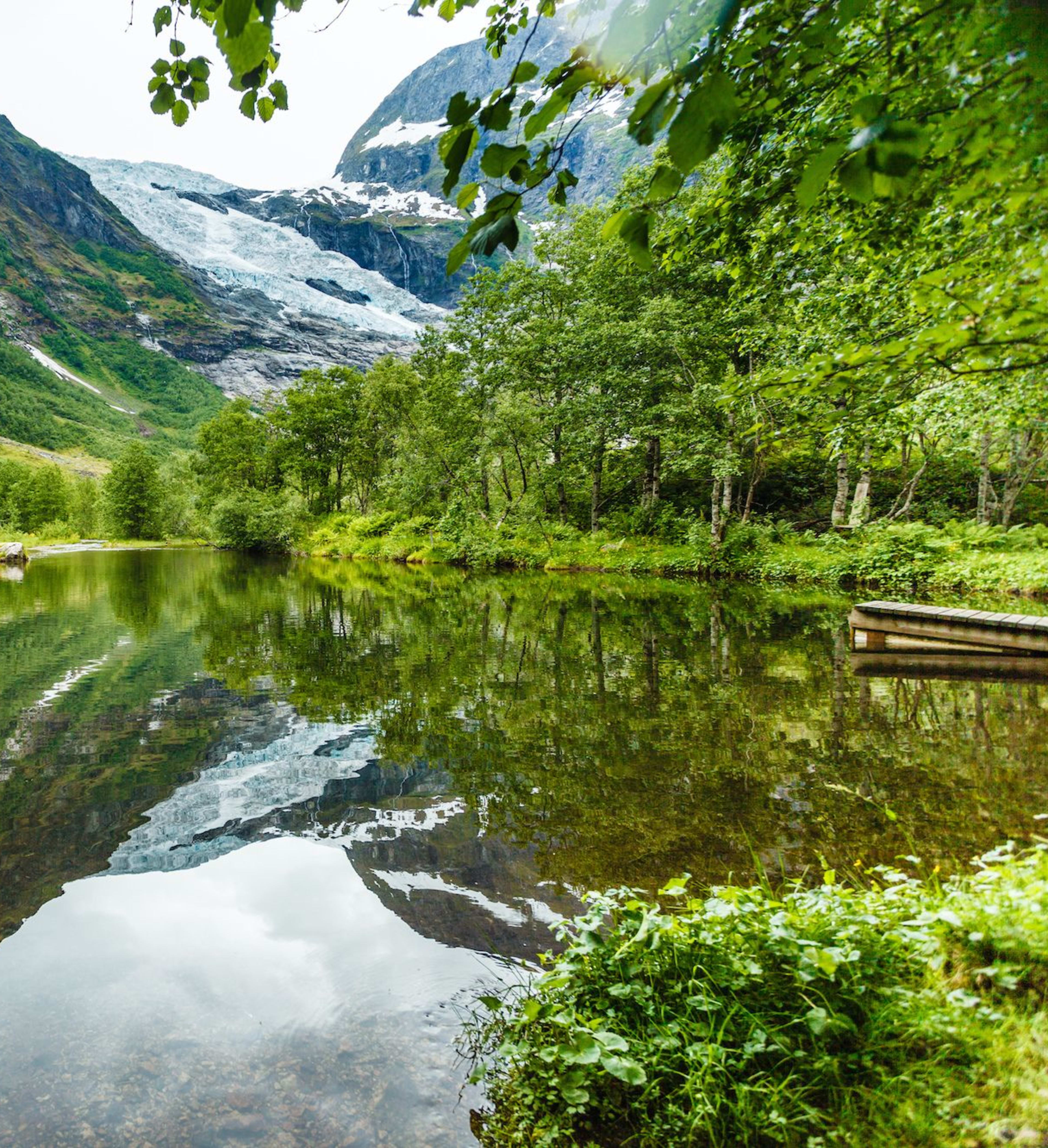Snow-capped mountains reflect on a still lake by a wooden dock.