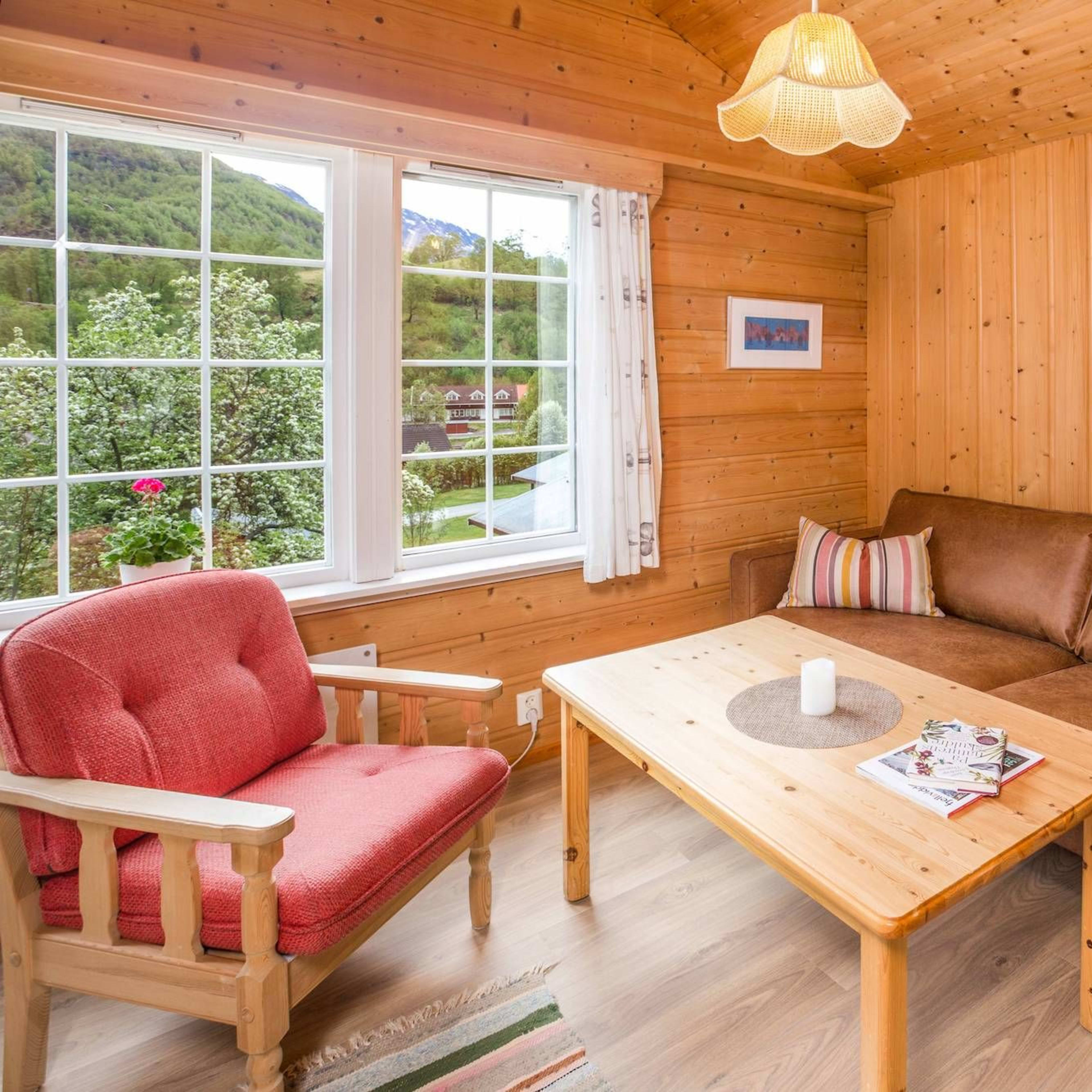 Wooden living room at Flåm Camping with sofa, chairs and coffee table and view of Flåm and the blossoming fruit trees